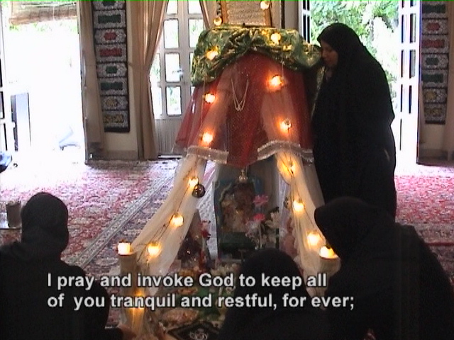 A woman rubbing the votive fabrics on the proxy shrine of Ruqayyeh on her cheek before the commemoration ceremony begins.